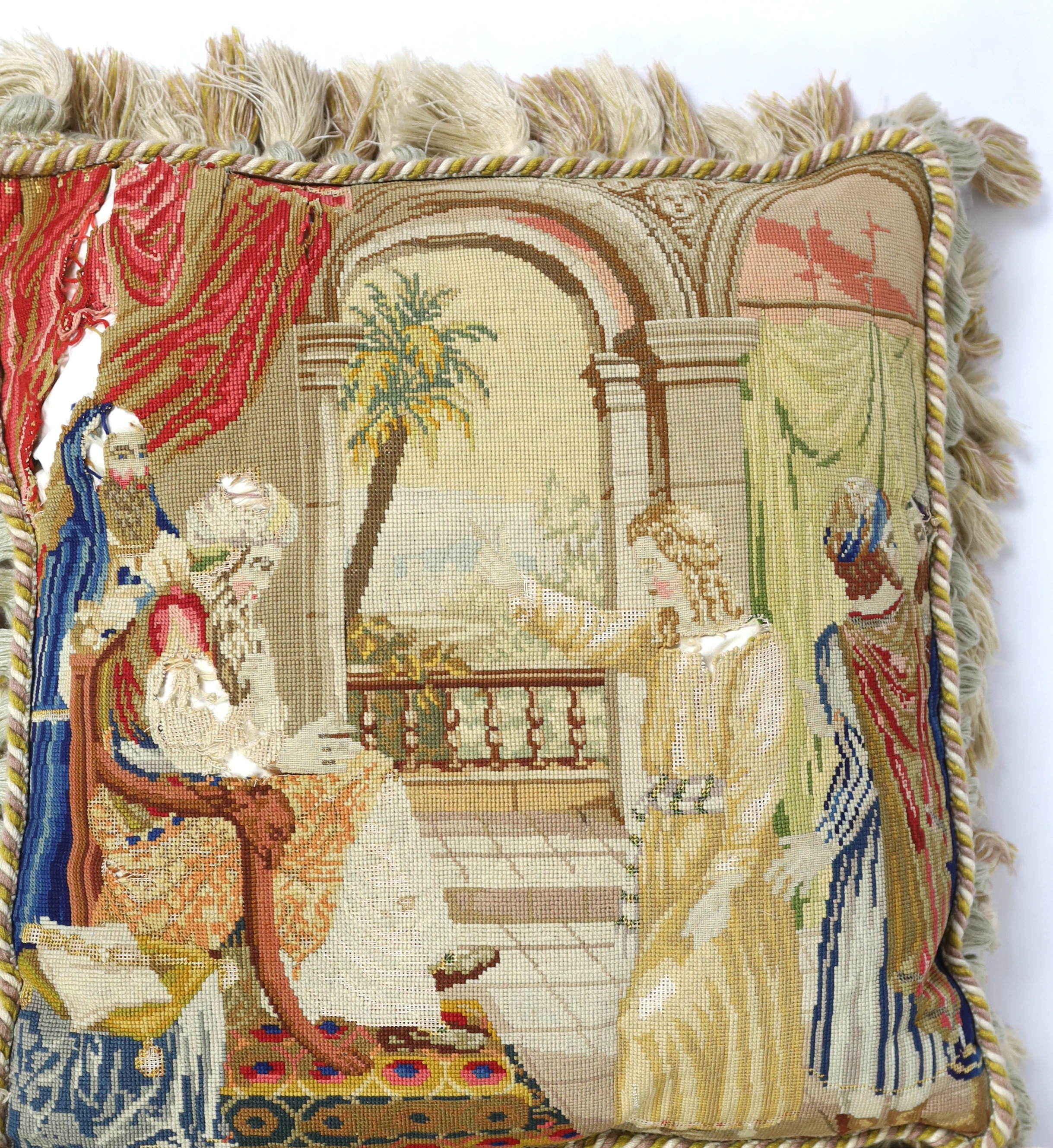 Three Victorian Berlin wool worked cushions possibly of classical biblical scenes, all three cushions edged with braiding and fringing, largest cushion 61cm wide, 65cm high